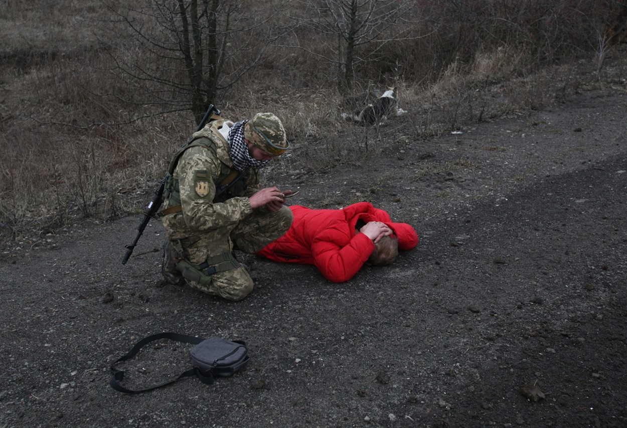 Солдат перевіряє телефон підозрілої людини, яка подавала сигнали на дорозі, на Луганщині