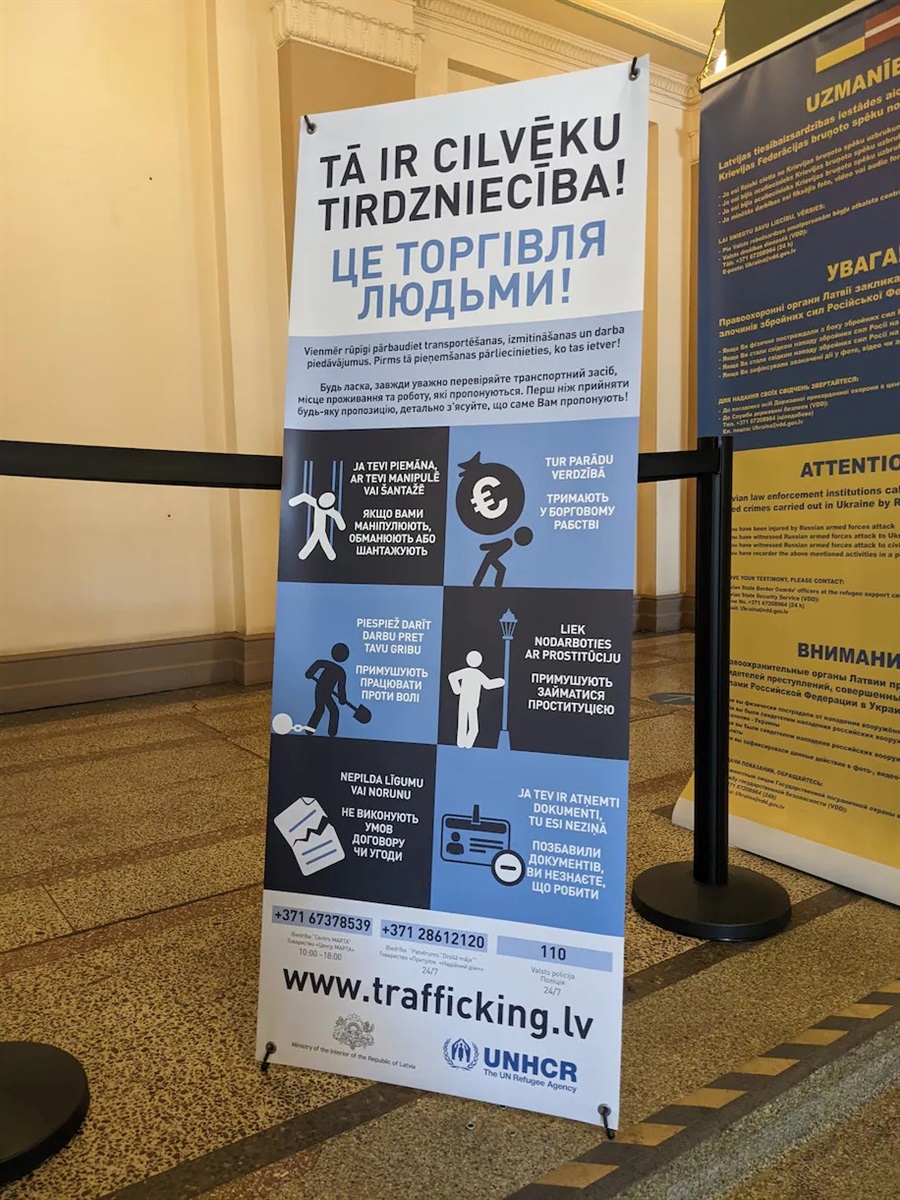 Банер з попередженням про небезпеку та різні види торгівлі людьми, номером телефону гарячої лінії українською та латиською мовами на вході до Центру підтримки українців у Латвії Ризької міської ради