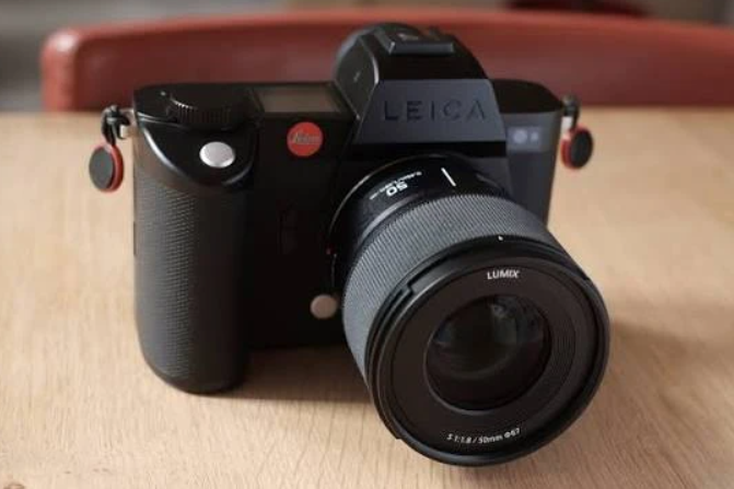 Безекранна чорна камера Leica SL з встановленим об'єктивом Lumix 50mm f/1.8 лежить на світлому дерев'яному столі.
