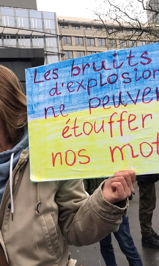 Оксана на мітингу у Франції. Напис на плакаті: “Звуки вибухів не можуть заглушити наші слова”